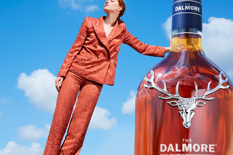 Woman leans on a bottle of whisky using perspective